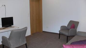 Una habitación con un escritorio, dos sillas grises, una puerta de madera y un sofá gris con cojines rosas.