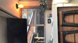Ein Zimmer mit an der Wand montiertem Fernseher, einem Fenster mit Blick nach außen und einer Holztür.