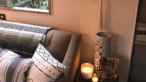 Ein gemütliches Zimmer mit einer Couch, einem dekorativen Schild, einer Topfpflanze und einer Kerze auf einem Beistelltisch.