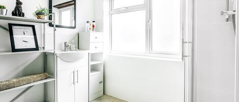 A modern bathroom with a white vanity, a mirror, a window, and a shower area.