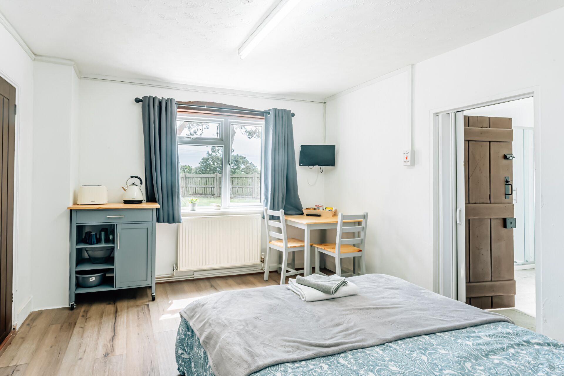 Ett sovrum med en säng, ett skrivbord, en stol, en tv och ett fönster med gardiner.