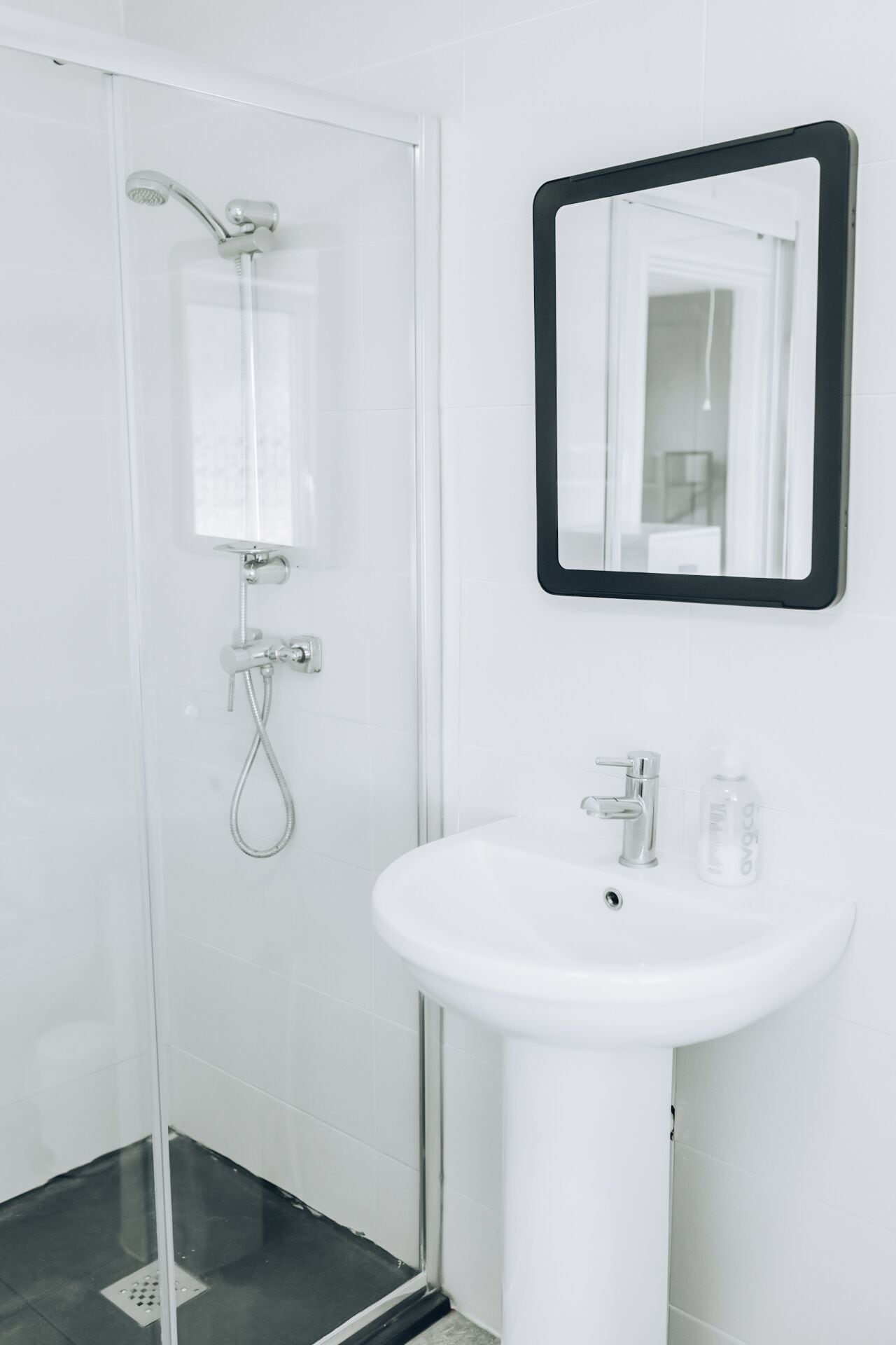 Een badkamer met een douchecabine van glas, een witte wastafel en een spiegel met een zwart frame.