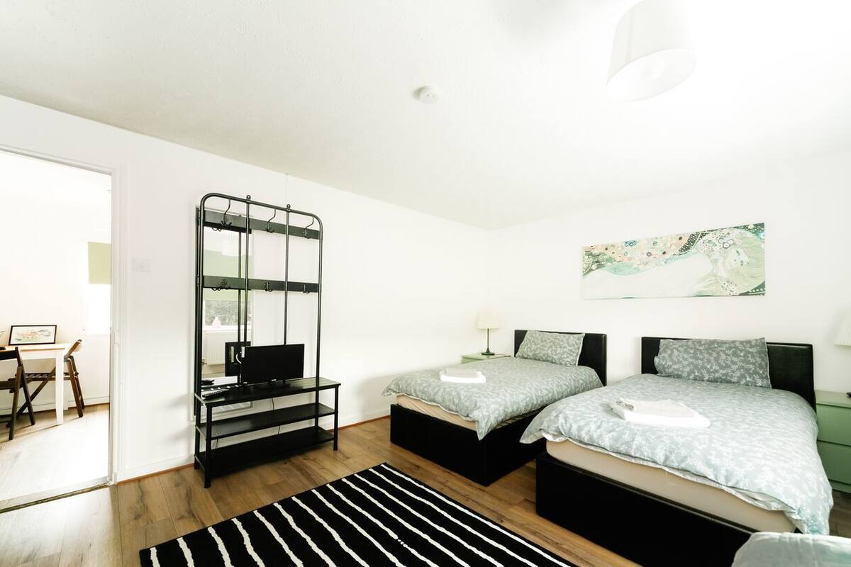 A modern bedroom with two beds, a black metal rack, a desk, and a painting on the wall.