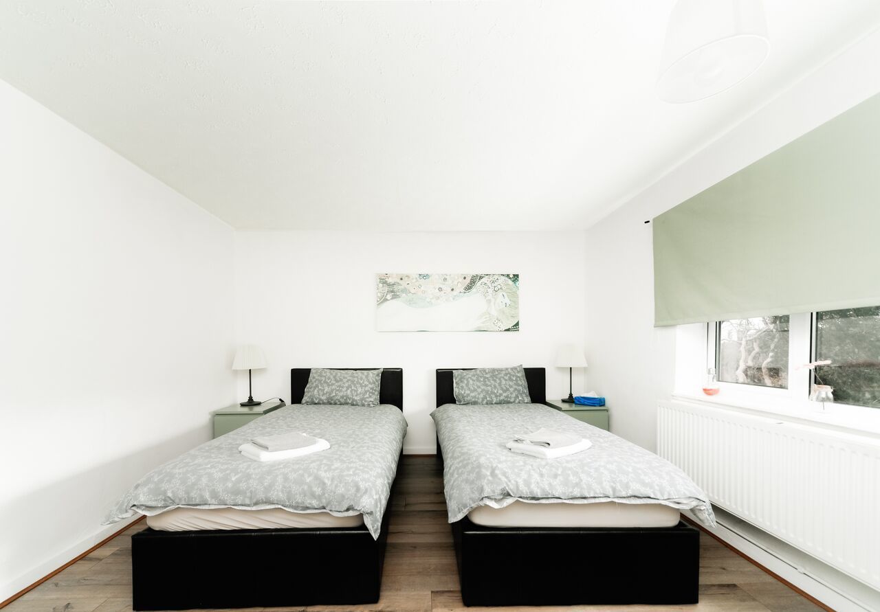 Une chambre avec deux lits, une fenêtre, un radiateur et un tableau accroché au mur.