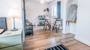 Une petite pièce comprenant un lit, un bureau, une chaise, une lampe, une petite table avec un four à micro-ondes et une statue.