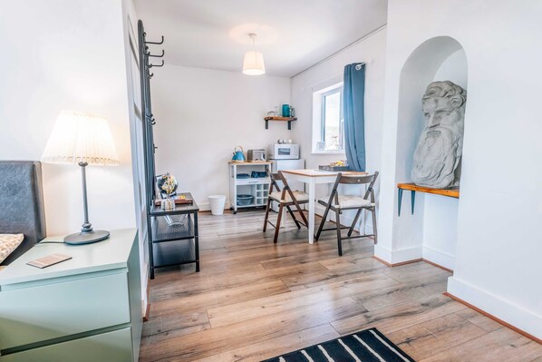 A compact room with a bed, a desk, a chair, a lamp, a small table with a microwave, and a statue. - Eastwood Lodge (Walberswick)