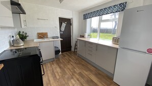 Une cuisine de taille réduite avec des meubles blancs, un lave-vaisselle noir et un plancher en bois.