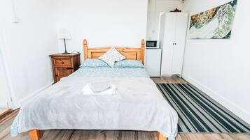 Un dormitorio ordenado con cama, mesita de noche, lámpara, armario y una obra de arte en la pared.