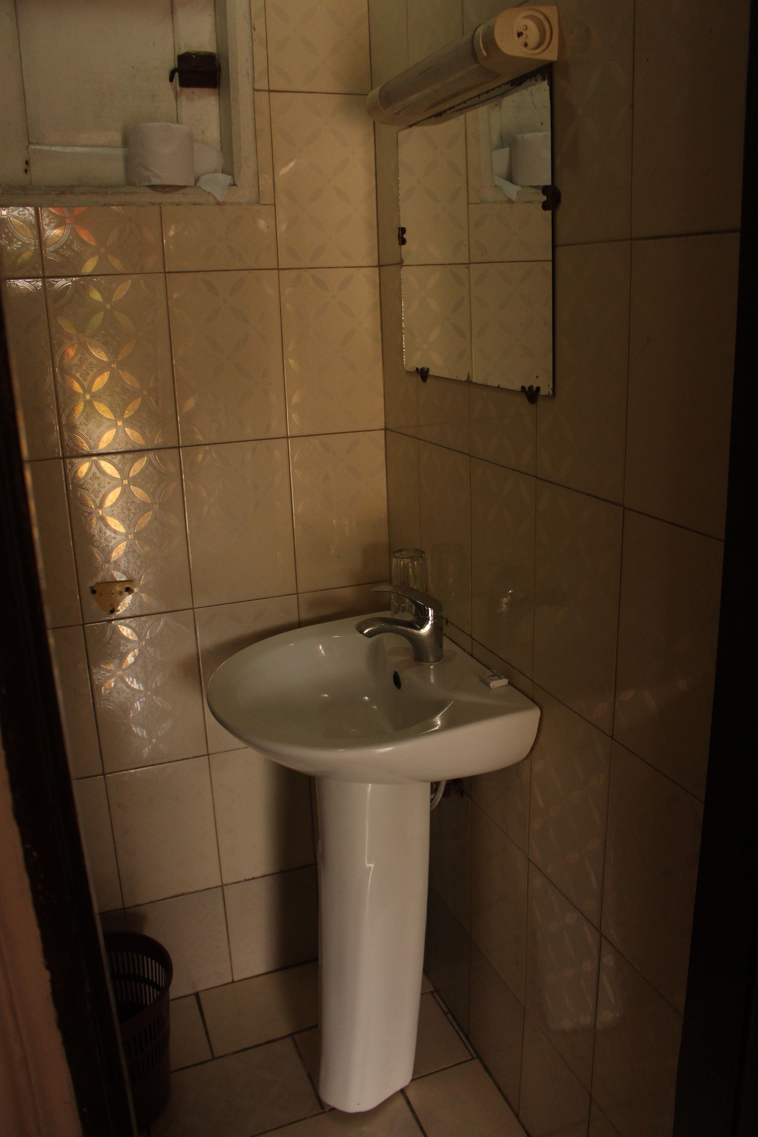 A bathroom with a white pedestal sink, a mirror, and a toilet paper holder on the wall.