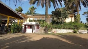 Zona de recepción con un cartel, un paseo cubierto y un edificio con pared de piedra y vegetación.