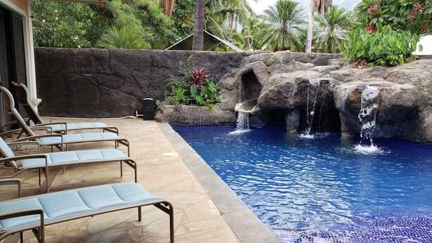 Ein Pool mit Wasserfall, umgeben von Liegestühlen und tropischen Pflanzen.