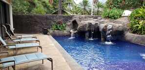 Ein Pool mit Wasserfall, umgeben von Liegestühlen und tropischen Pflanzen.