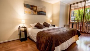 Una camera da letto con un letto grande, due comodini con lampade, un quadro appeso alla parete e vista attraverso una finestra con ringhiera in metallo.