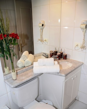 A bathroom with a marble sink, two hair dryers mounted on the wall, a toilet, and a vase with red roses.