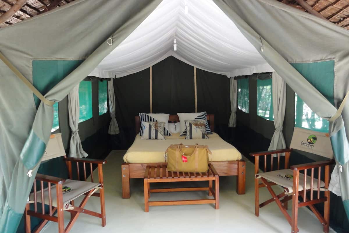 A tented accommodation with a bed, two wooden chairs, and a bench.