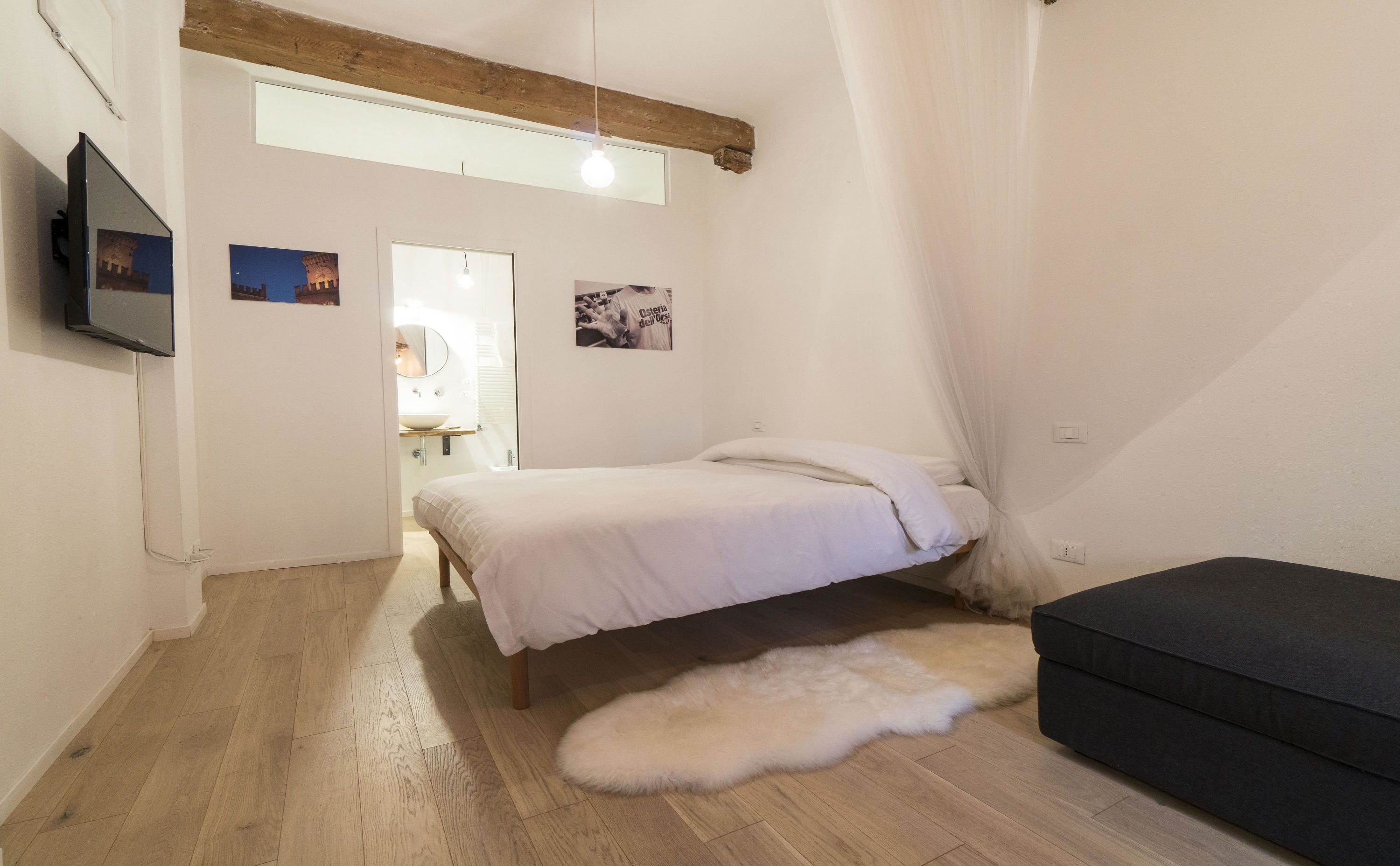 A bedroom with a bed, a sofa, a fur rug, a TV, and a window with curtains.