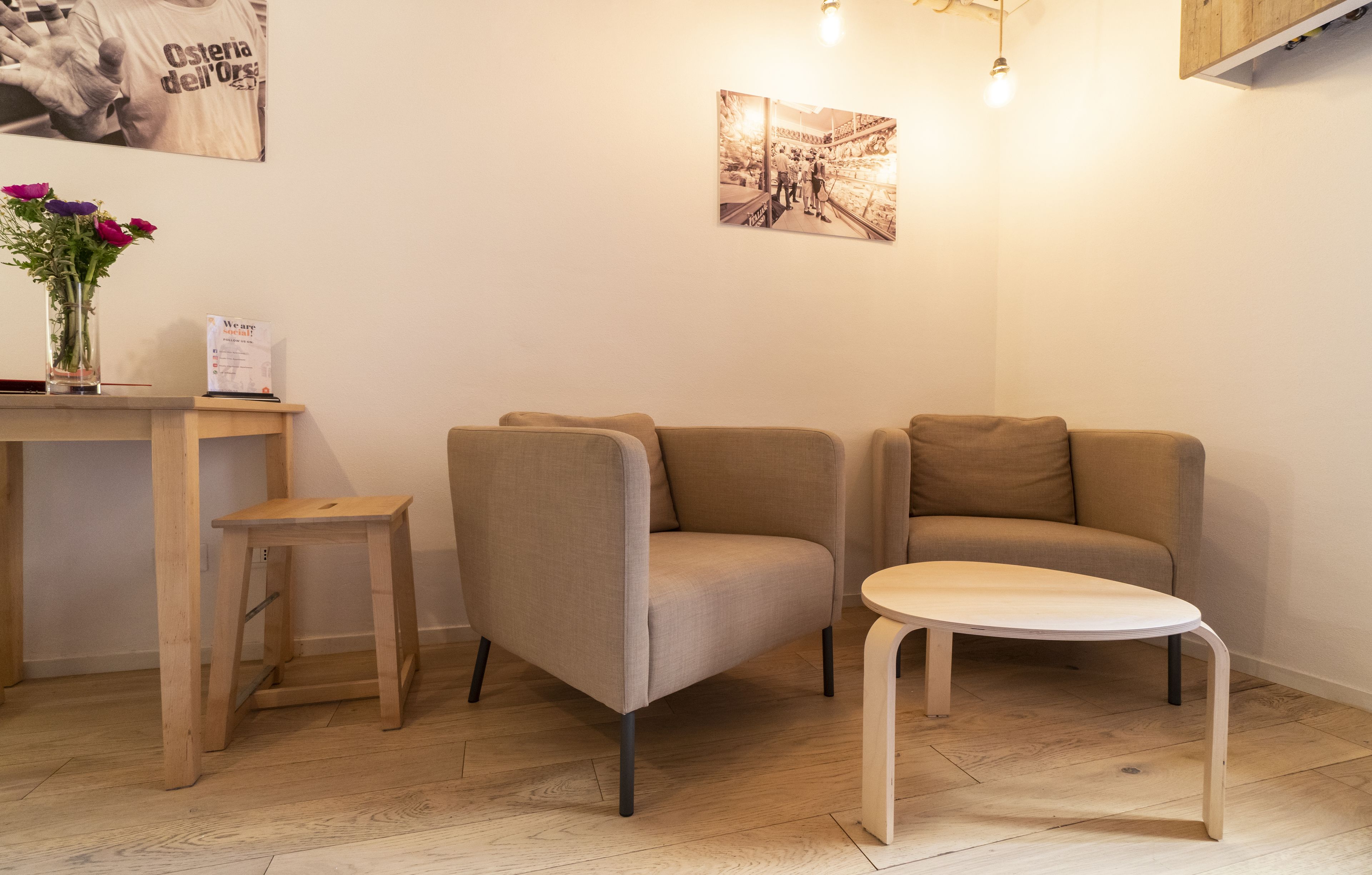 Ein modernes, minimalistisches Zimmer mit Holzboden, zwei beigefarbenen Sesseln, einem kleinen Holztisch und einem Holzschemel.