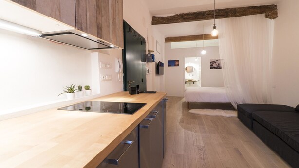 A compact kitchen with a wooden countertop, built-in appliances, and a view into a bedroom with a bed and a window. - Lovely Studio D'azeglio (Bologna)