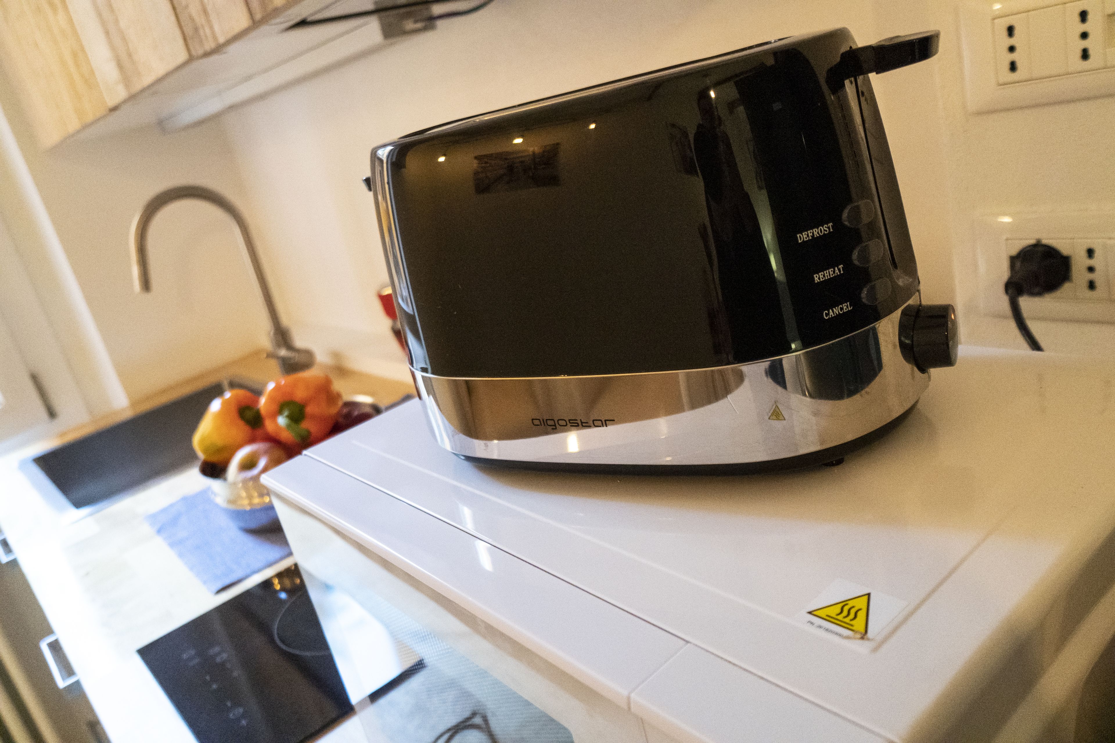 A kitchen with a toaster on the counter, a sink, and a fruit bowl with apples and oranges.