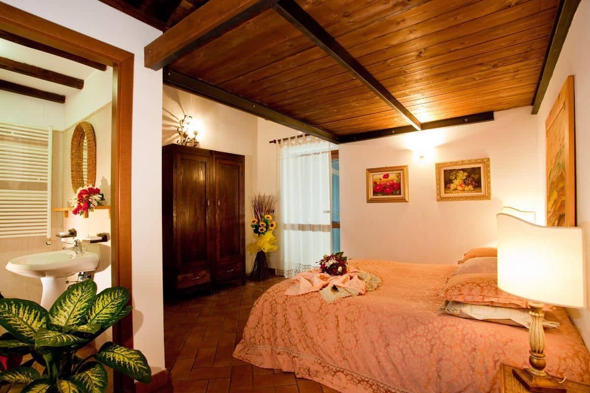 A cozy bedroom with a wooden ceiling, a bed with a floral bedspread, a bedside lamp, and a wall-mounted painting.
