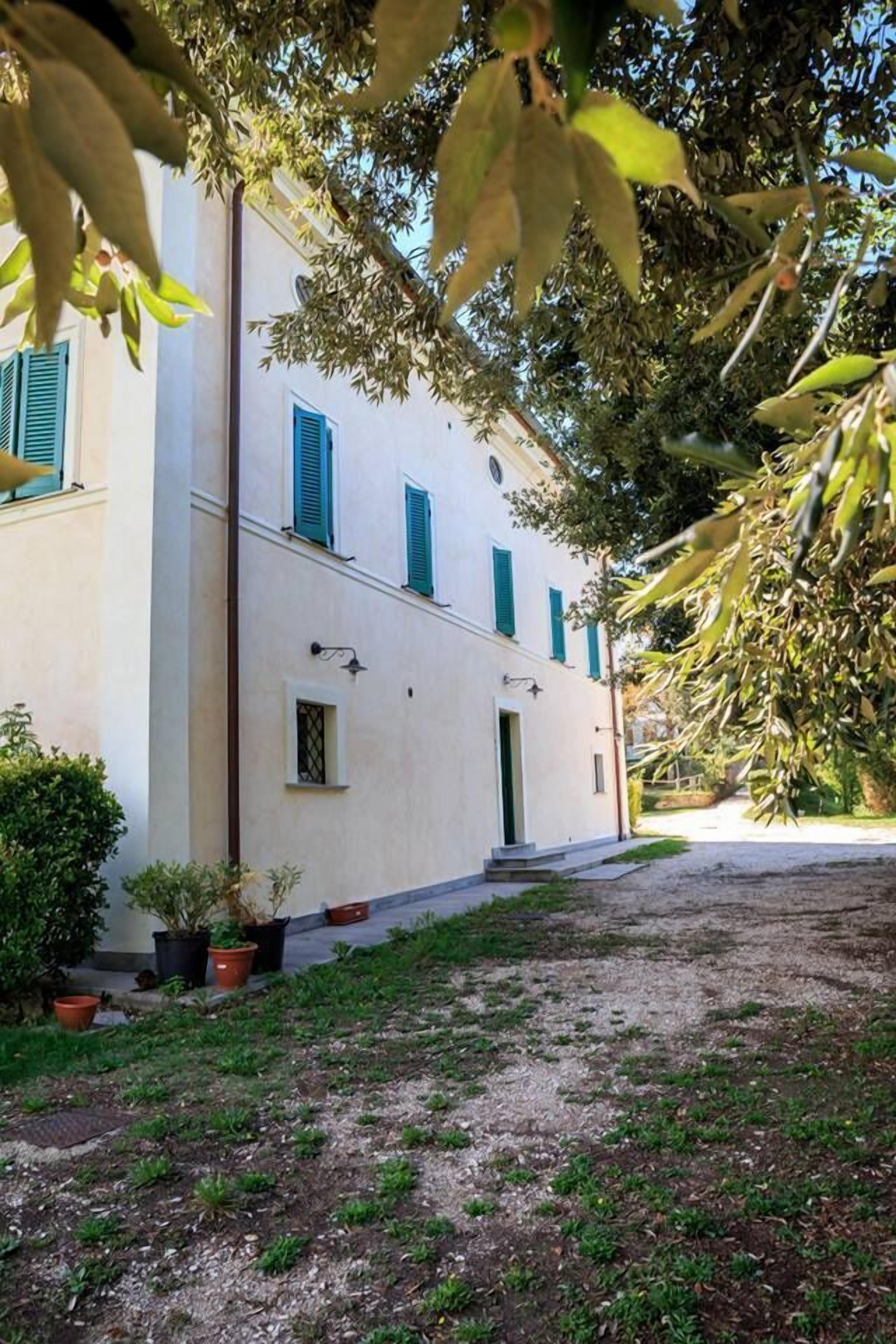 Un edificio con fachada blanca, contraventanas verdes y un acceso empedrado.
