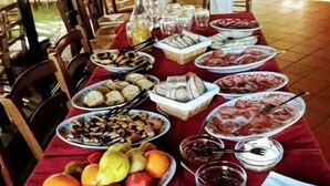 Una mesa dispuesta con diversos platos, entre ellos frutas, pan y salsas, en un comedor con sillas y mesas.