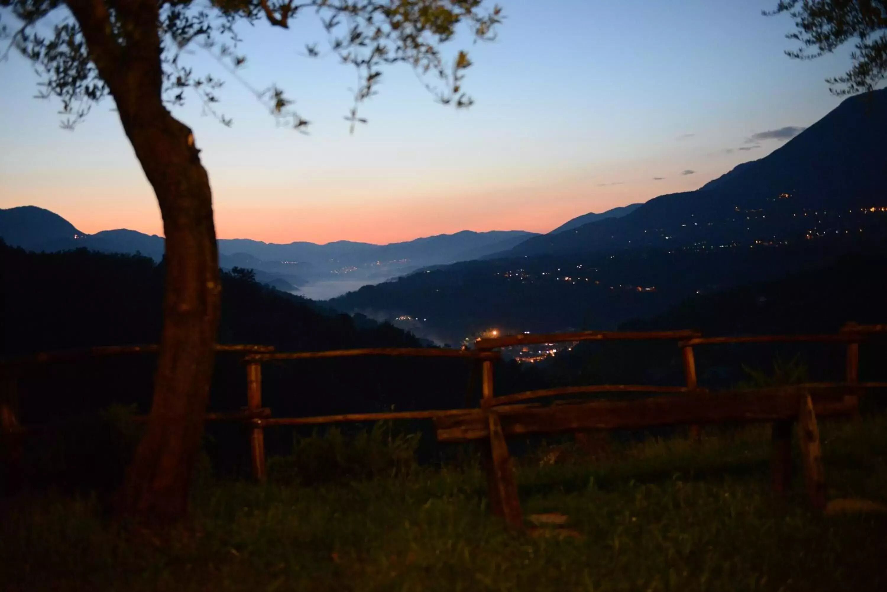 Una valla de madera en un entorno natural, con vistas a montañas distantes y luces en el valle.