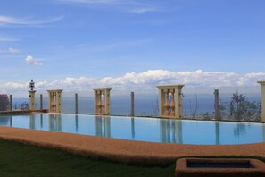 Une piscine avec vue sur l’océan, entourée de colonnes et agrémentée d’un lampadaire.