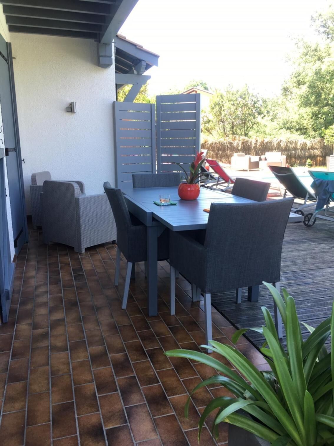 Een terras buiten met een tafel en stoelen, een potplant en een zwembad op de achtergrond.