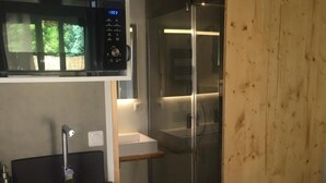 A compact kitchen with a microwave, sink, and wooden sliding door leading to a bathroom. - Villa Andernos (Andernos-les-Bains)