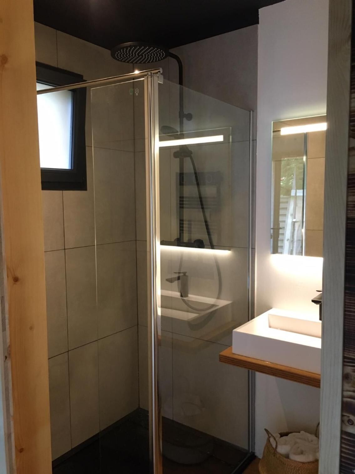 Ein modernes Badezimmer mit einer in Glas eingefassten Dusche, einem weißen Waschbecken und einem Spiegel darüber.