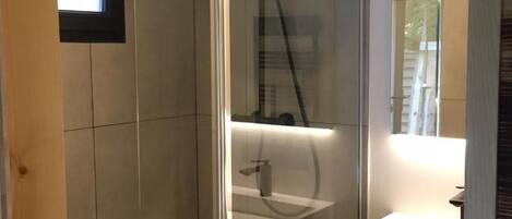 Ein modernes Badezimmer mit einer in Glas eingefassten Dusche, einem weißen Waschbecken und einem Spiegel darüber.