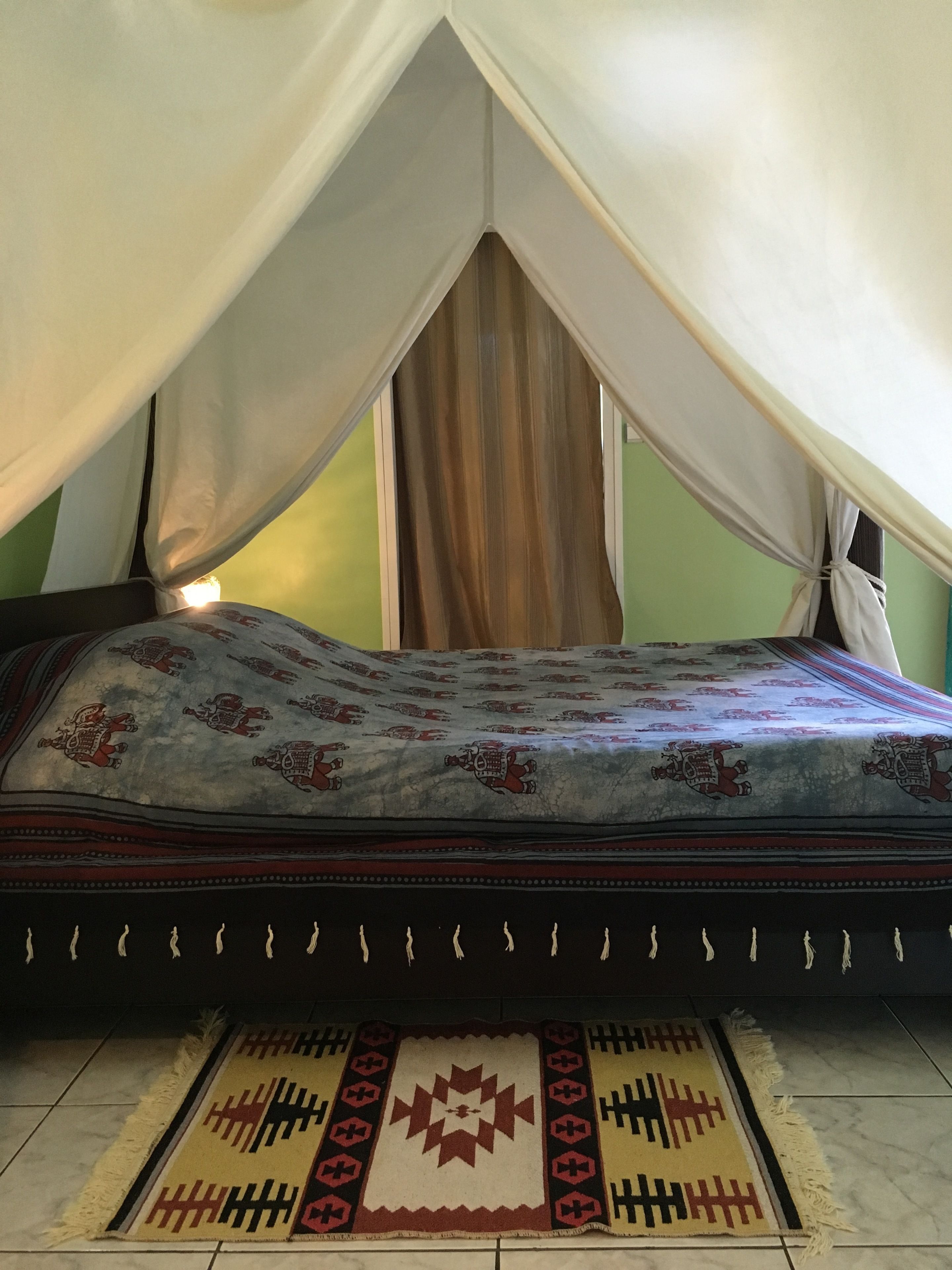 Een bed met hemelbed, een bed met een patroonbedover en een decoratief vloerkleed op een betegelde vloer.
