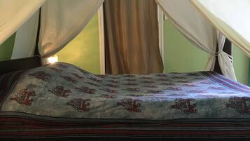 Una cama con dosel, una colcha estampada y un tapete decorativo sobre suelo de baldosas.