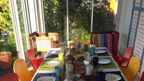 Uma mesa de jantar posta com pratos, copos e um jarro, cercada por cadeiras coloridas.