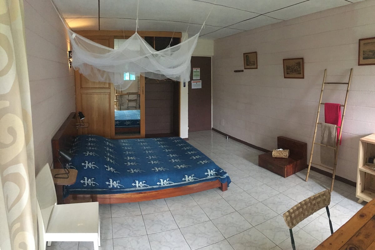 A bedroom with a bed, a chair, a table, a ladder, and a wardrobe.