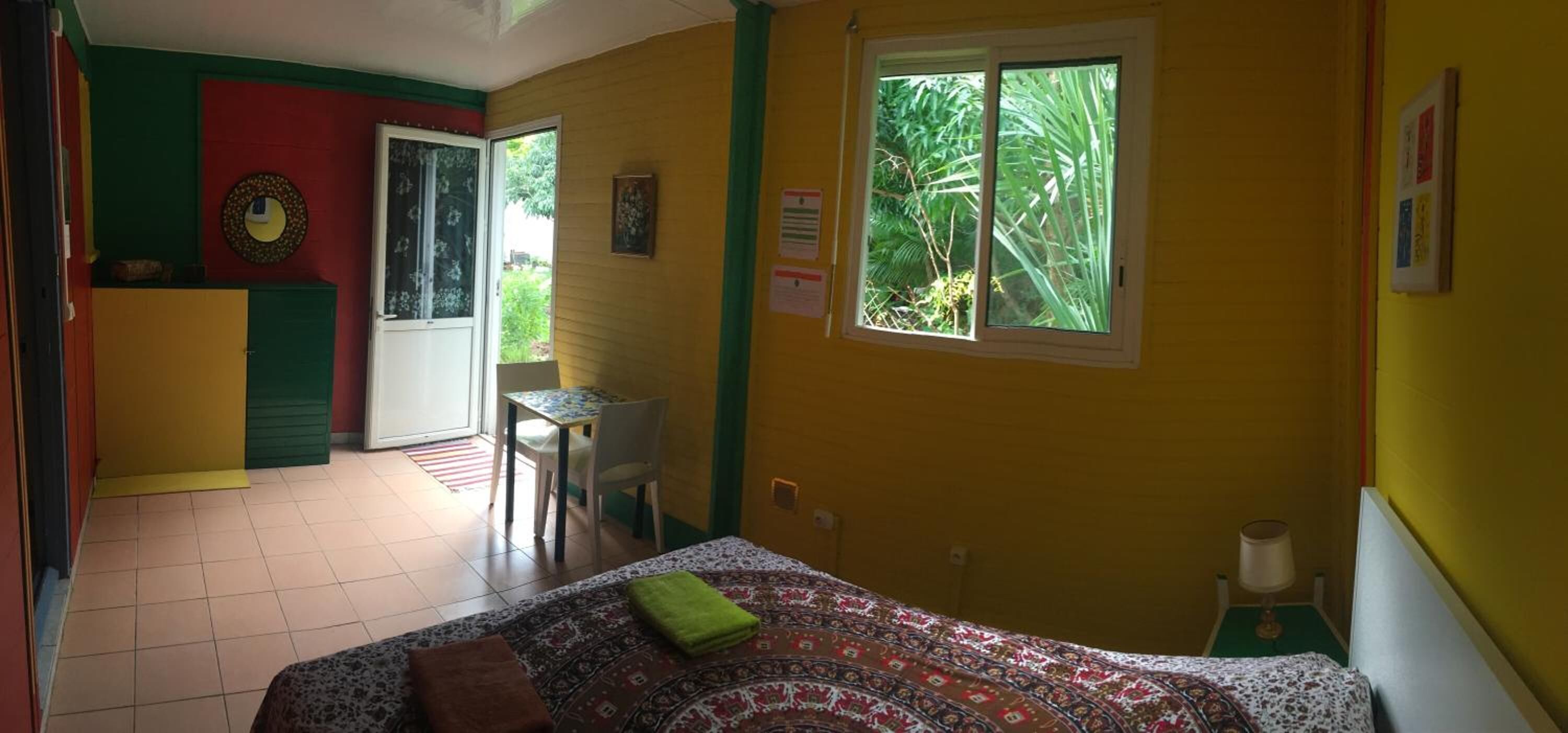 Una habitación con cama, una mesita y una silla. Se ve follaje a través de la ventana.