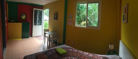 Una habitación con cama, una mesita y una silla. Se ve follaje a través de la ventana.