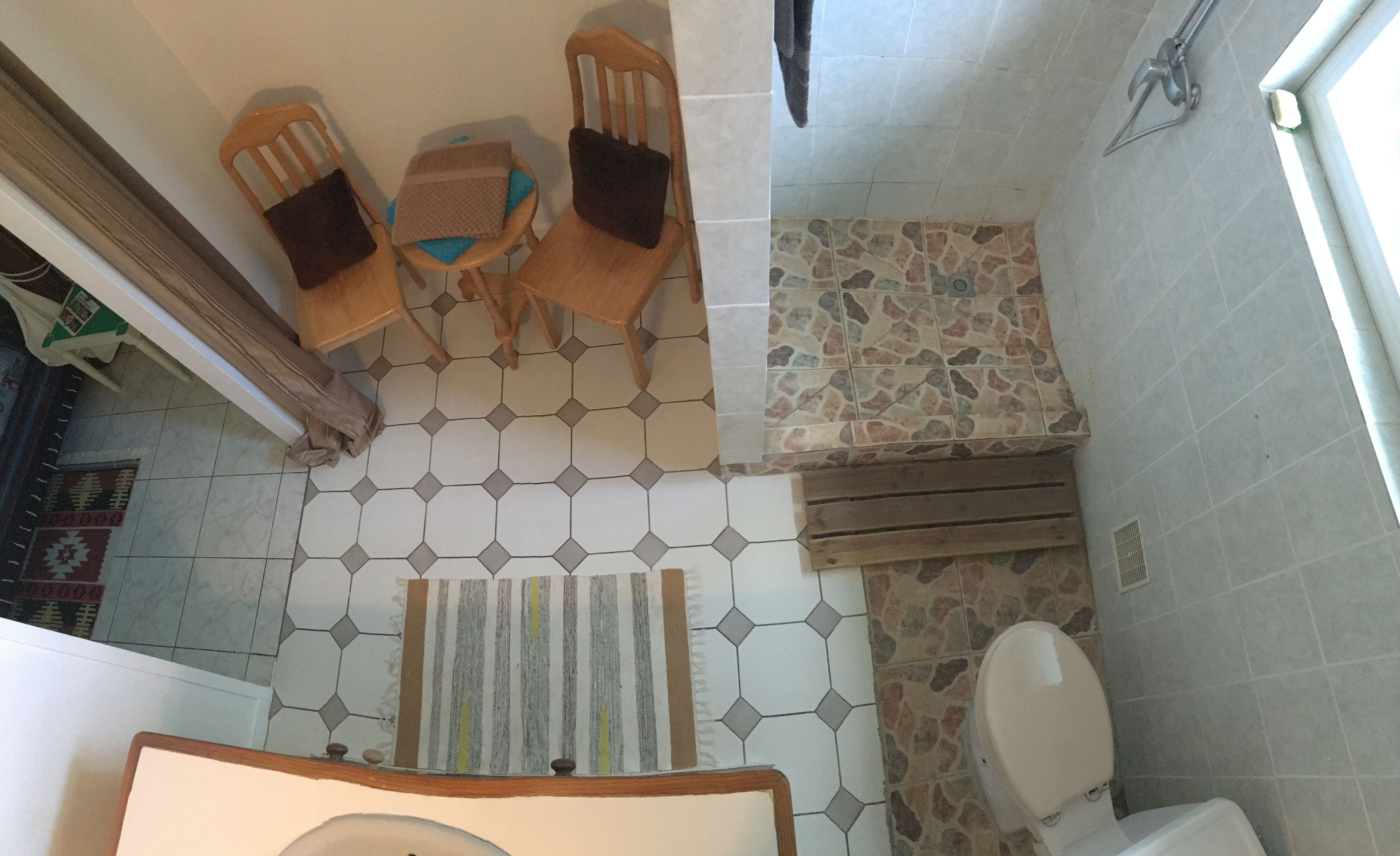 Een badkamer met betegelde vloer, toilet, douche en een klein tafeltje met stoelen.