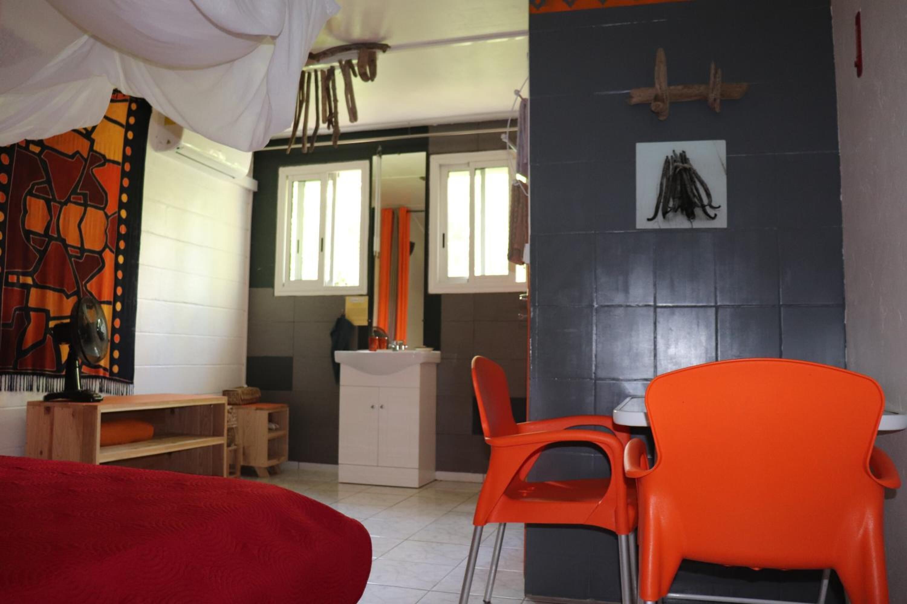 Een kamer met een bed, een houten bureau, een witte kast, een oranje stoel en een spiegel.