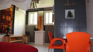 Een kamer met een bed, een houten bureau, een witte kast, een oranje stoel en een spiegel.
