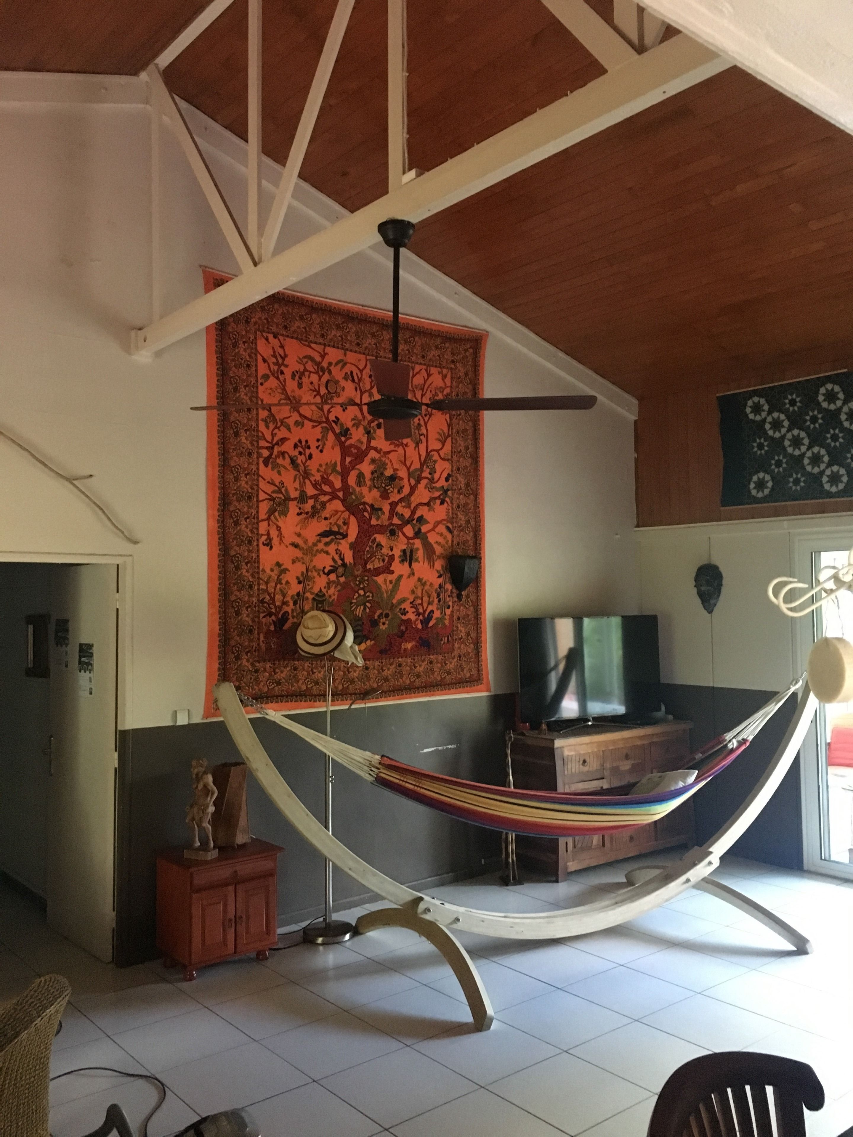Eine Hängematte in einem Zimmer mit Deckenventilator, Fernseher und einem gemusterten Wandteppich.