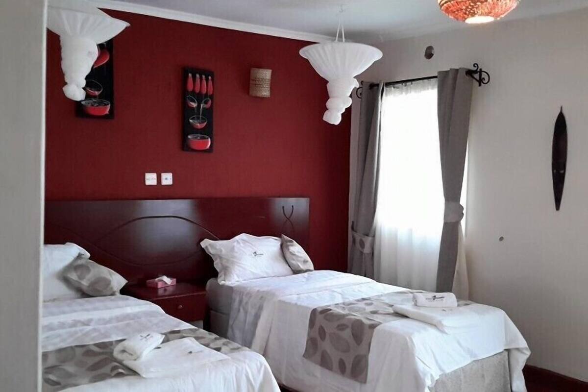 Una habitación de hotel con dos camas, una pared de acento roja y una ventana con cortinas.