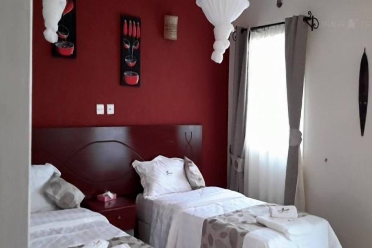 Habitación de hotel con dos camas individuales, una pared de acento roja y una ventana con cortinas.