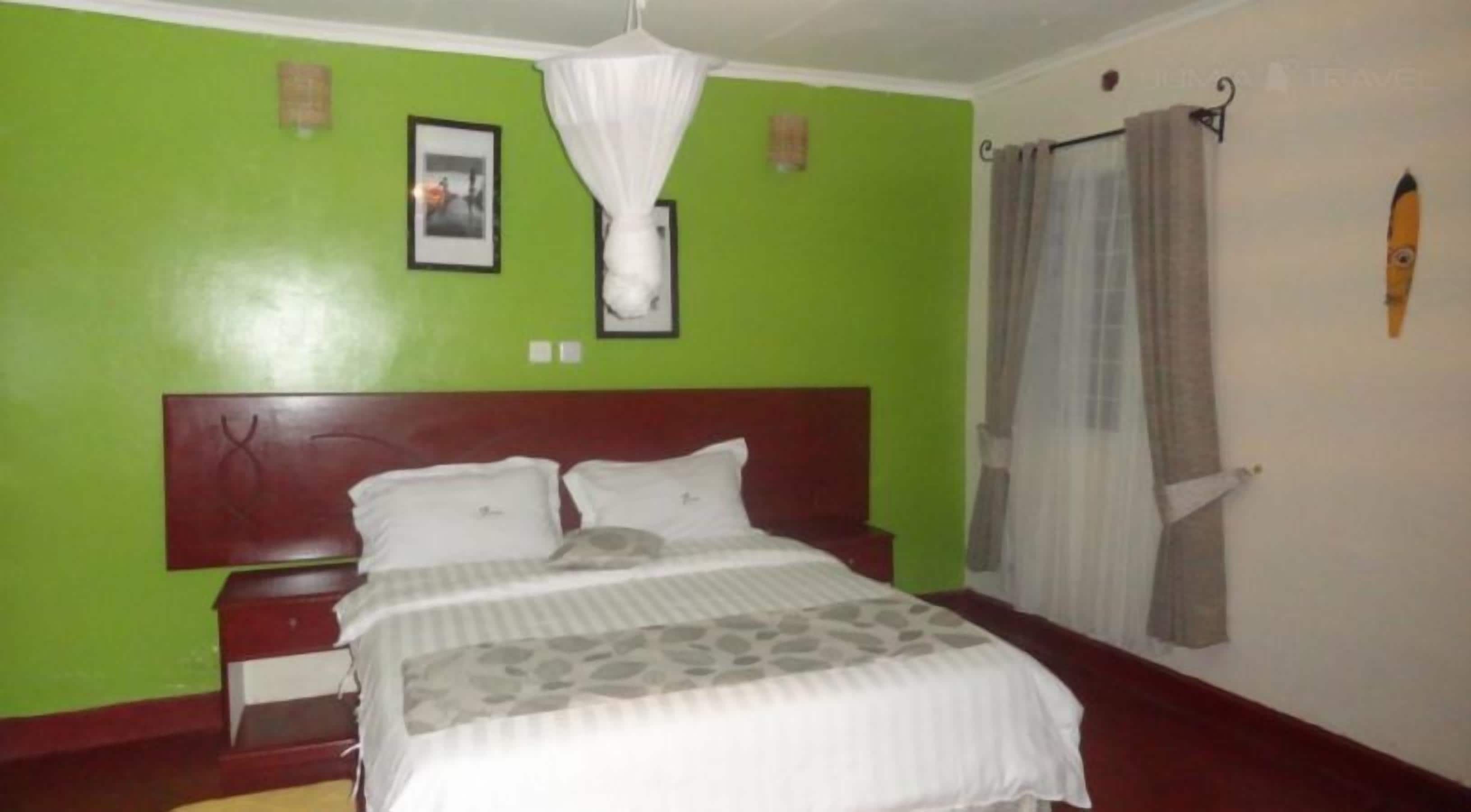 Une chambre d’hôtel avec un lit, une table de chevet, un mur vert, un tableau encadré et une fenêtre avec des rideaux.