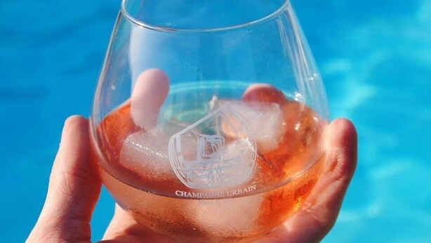 A hand holding a glass of champagne with ice cubes. - Champagne Urbain (Baroville)