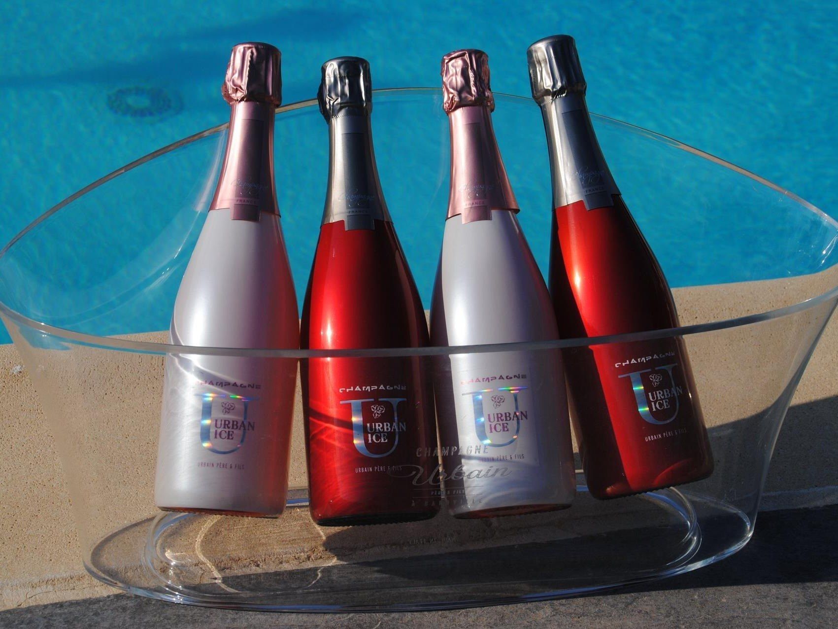 Four bottles of Urban Ice champagne in a clear glass holder by a pool.