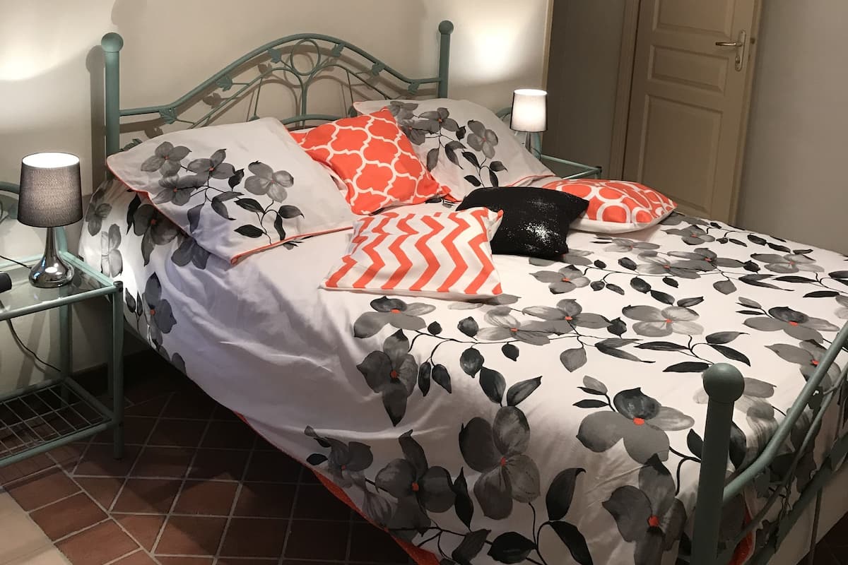 A bed with floral bedding, a lamp, and a door in a room with tiled flooring.