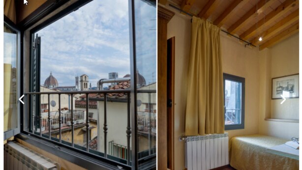 Una habitación con un amplio ventanal que ofrece vistas a un paisaje urbano, un radiador, una cama con cabecera y un techo de madera.