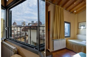 Una habitación con un amplio ventanal que ofrece vistas a un paisaje urbano, un radiador, una cama con cabecera y un techo de madera.